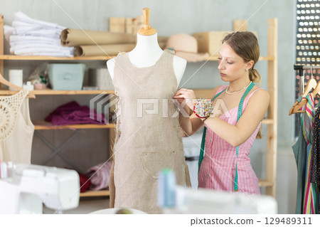 Woman seamstress adjusts clothes on mannequin 129489311