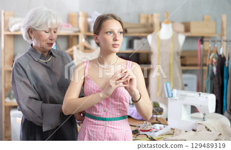 Mature dressmaker measuring client Mature dressmaker measuring client 129489319