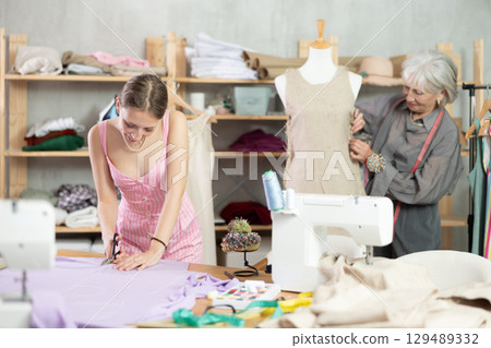 young dressmaker helps a seamstress with sewing clothes young dressmaker helps a seamstress with sewing clothes 129489332