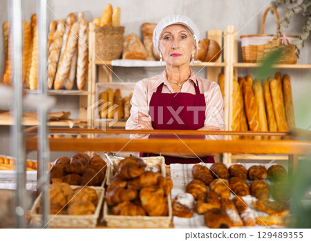 Senior female baker worker sells croissants, shows many different crescent rolls Senior female baker worker sells croissants, shows many different crescent rolls 129489355