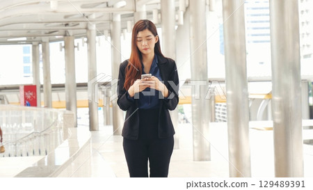 Business woman using smartphone shopping online, call, texting message internet technology lifestyle. Asian woman using cellphone walking on city street. Smart phone smart confident woman modern city Business woman using smartphone shopping online, call, texting message internet technology lifestyle. Asian woman using cellphone walking on city street. Smart phone smart confident woman modern city 129489391