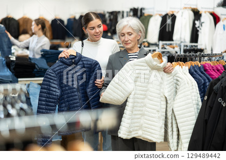 Two women choosing white jacket in clothing store Two women choosing white jacket in clothing store 129489442