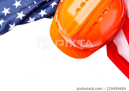 Orange hard hat resting next to American flags, isolated on white, PNG 129489484