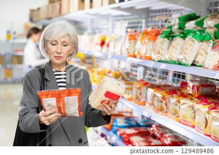 Senior woman in supermarket buys daily groceries, pasta Chinese noodles 129489486