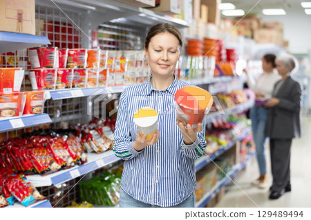 In store near window, woman customer examines package of instant soup in bowl 129489494