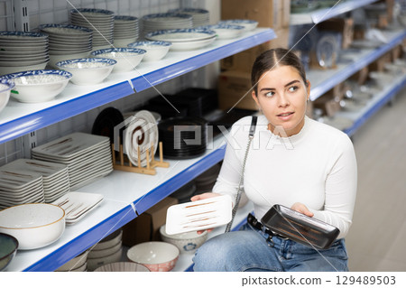 Young woman in supermarket is choosing square plates 129489503