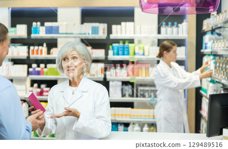 Senior woman apothecary hold package with cream and talks with man client about nuances of care 129489516