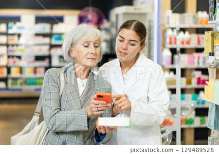 Old woman showing to young female pharmacist QR-code of product on her smartphone Old woman showing to young female pharmacist QR-code of product on her smartphone 129489528
