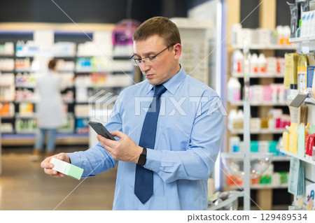In pharmacy male visitor scan bar code and reads composition of medicinal ointment 129489534