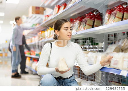 Interested girl reading label on packages of Asian noodles in supermarket 129489535