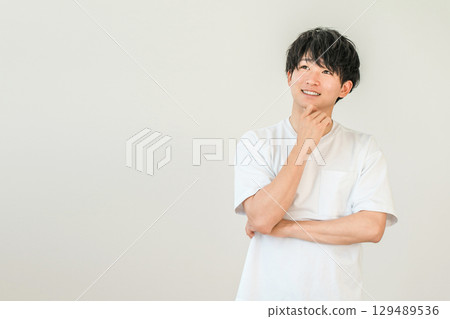 A smiling young Asian man resting his chin on his hands (imagination, memories, thoughts, ideas, future, dreams, delusions) 129489536