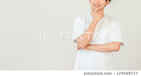 A smiling young Asian man resting his chin on his hands (imagination, memories, thoughts, ideas, future, dreams, delusions) 129489537