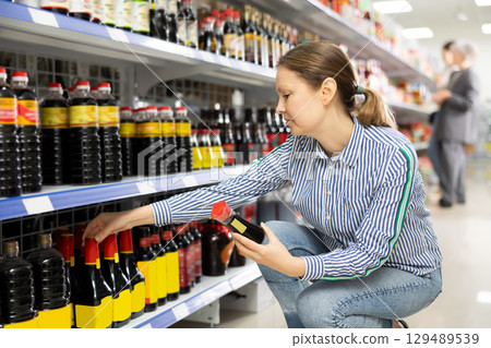 Interested female shopper choosing Chinese soy sauce in Asian store Interested female shopper choosing Chinese soy sauce in Asian store 129489539