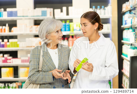 Girl apothecary hold package with cream and talks with senior woman client about nuances of care 129489714