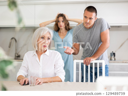 Couple quarreling with elderly woman in kitchen Couple quarreling with elderly woman in kitchen 129489739