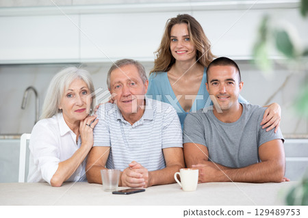 Portrait of a happy family of four sitting together at kitchen table Portrait of a happy family of four sitting together at kitchen table 129489753