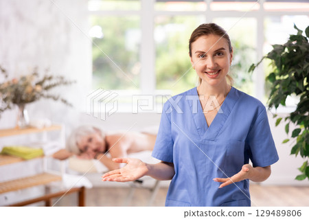 Smiling young professional masseuse inviting to cozy massage room 129489806