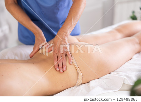 Masseuse hands doing back pain relief massage to young woman 129489863