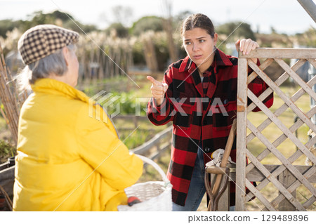Two angry casual women neighbors of different ages arguing during the vegetable garden season on sunny day of spring 129489896
