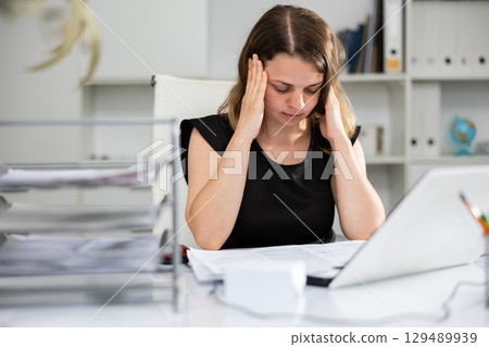 Upset woman working with laptop and papers at office Upset woman working with laptop and papers at office 129489939