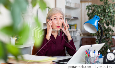 Stressed mature woman working in office Stressed mature woman working in office 129490179