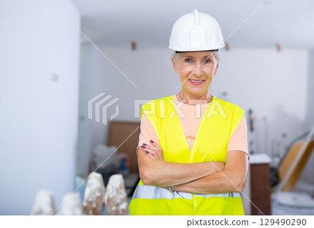 Portrait of positive builder woman in protective helmet and yellow vest in renovated room 129490290