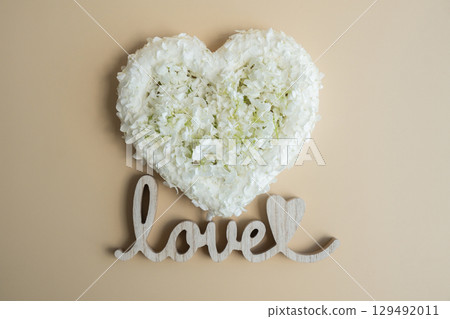Symbol of love beautiful flower petals in heart shape with Wooden word LOVE in beige background. Creative concept of St Valentines day, weeding romantic date or anniversary. Copy space 129492011