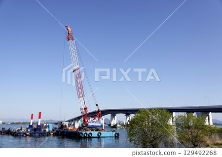 Under a clear blue sky, Lake Biwa Bridge and a crane barge in operation 129492268
