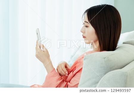 觀看在沙發的一位小姐一個智能手機 129493597