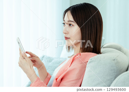 A young lady watching a smartphone on a sofa A young lady watching a smartphone on a sofa 129493600