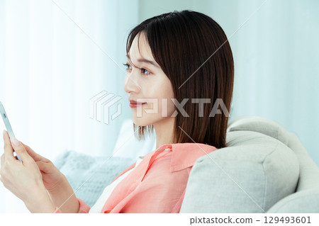 A young lady watching a smartphone on a sofa A young lady watching a smartphone on a sofa 129493601