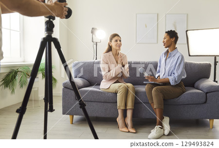 Businesswoman giving interview to journalist in front of camera sitting on sofa Businesswoman giving interview to journalist in front of camera sitting on sofa 129493824