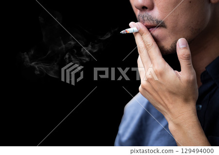 Side view of young bearded man smoking cigarette on black background. 129494000