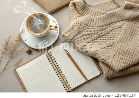 Cozy Workspace with Coffee, Notebook, Sweater, and Dried Flowers on Gray Surface 129497137