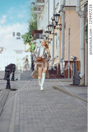 Young woman strolls along a charming cobblestone street in a quaint town during sunny weather 129497216