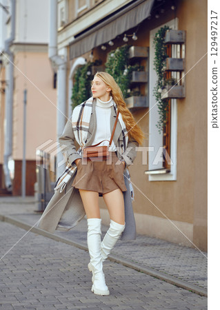 Stylish woman walking on a cobblestone street in a trendy outfit during daytime in an urban setting 129497217