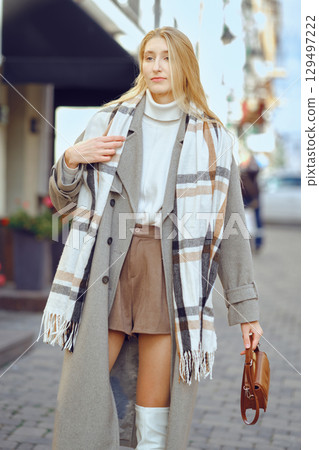 Stylish young woman in a coat and scarf walking along a cobblestone street during daylight Stylish young woman in a coat and scarf walking along a cobblestone street during daylight 129497222