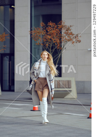 A fashionable woman walks confidently on a city street during autumn, showcasing her stylish outfit 129497229