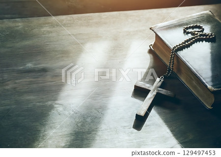 Wooden Cross and Open Bible on Table with Soft Light Illuminating the Scene Wooden Cross and Open Bible on Table with Soft Light Illuminating the Scene 129497453