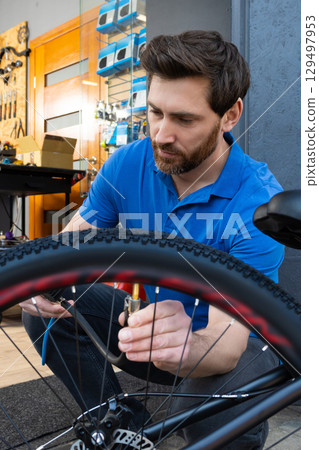 Man in polo shirt using compressor to inflate bicycle tire at service station Man in polo shirt using compressor to inflate bicycle tire at service station 129497953