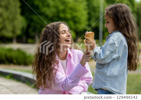 Happy mother and daughter eating ice cream cones outdoors Happy mother and daughter eating ice cream cones outdoors 129498142