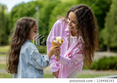 Young mom and daughter laughing with ice cream cones in park Young mom and daughter laughing with ice cream cones in park 129498143
