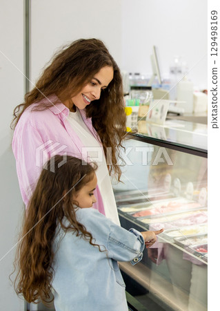 Smiling mother and daughter choosing ice cream in modern dessert shop Smiling mother and daughter choosing ice cream in modern dessert shop 129498169