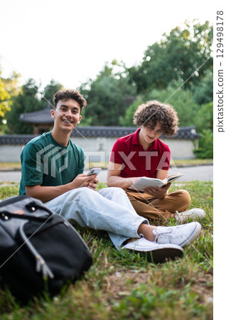 Teens sitting on the grass in the park and enjoying time together Teens sitting on the grass in the park and enjoying time together 129498178