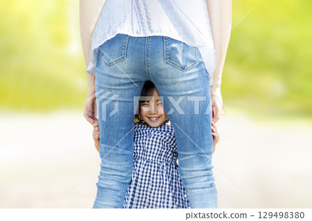Smiling little girl peeking between her mother's legs 129498380