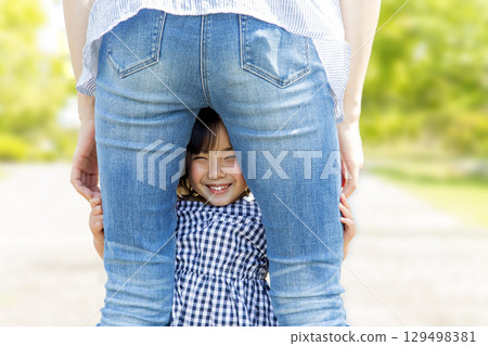 Smiling little girl peeking between her mother's legs 129498381