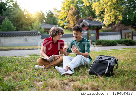 Two teens sitting on the grass and reading books while preparing for lessons 129498438