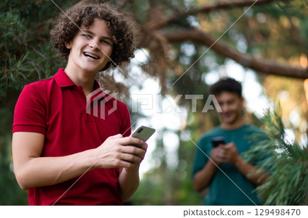 Two teens with phone in hands in the park Two teens with phone in hands in the park 129498470