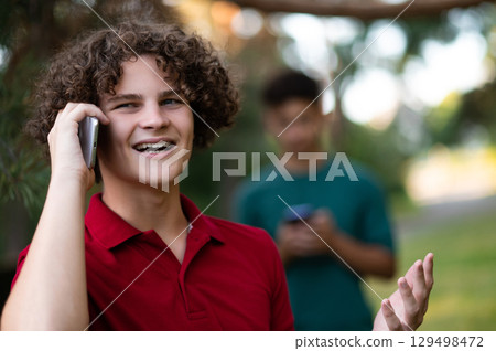 Curly-haired teen talking on the phone while his friend texting and smiling 129498472