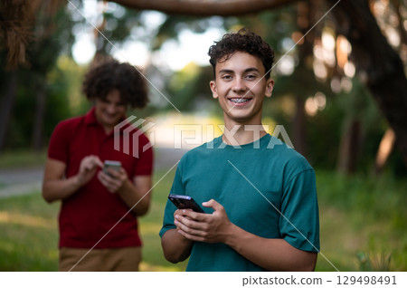 Teens with phones in hands spending time together in the park Teens with phones in hands spending time together in the park 129498491